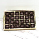 Box of 24 pieces of rounded dome shaped dark chocolates on a marble surface with a white background